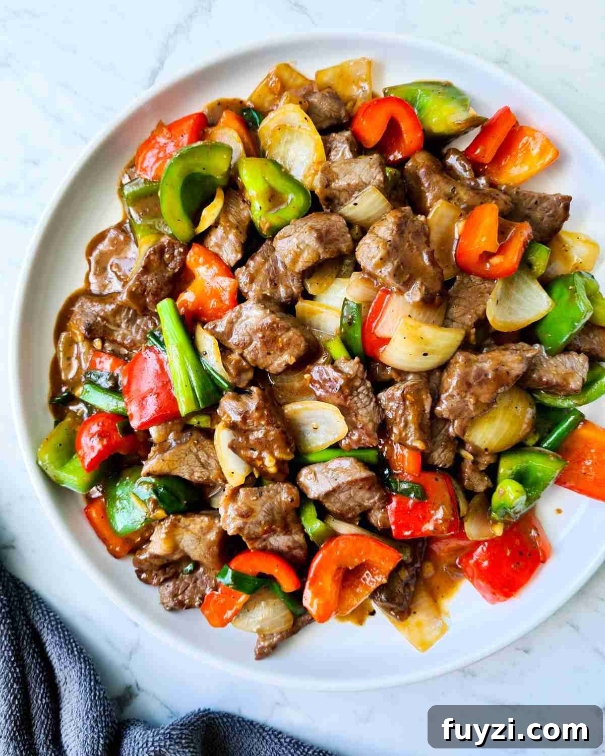 Restaurant-Style Black Pepper Beef Stir-Fry 3 beef cubes and vegetables in a black pepper sauce on a round white plate
