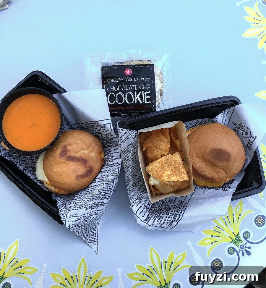 two trays with gluten-free grilled cheese on round buns next to tomato soup and a packaged gluten-free chocolate chip cookie at Disneyland