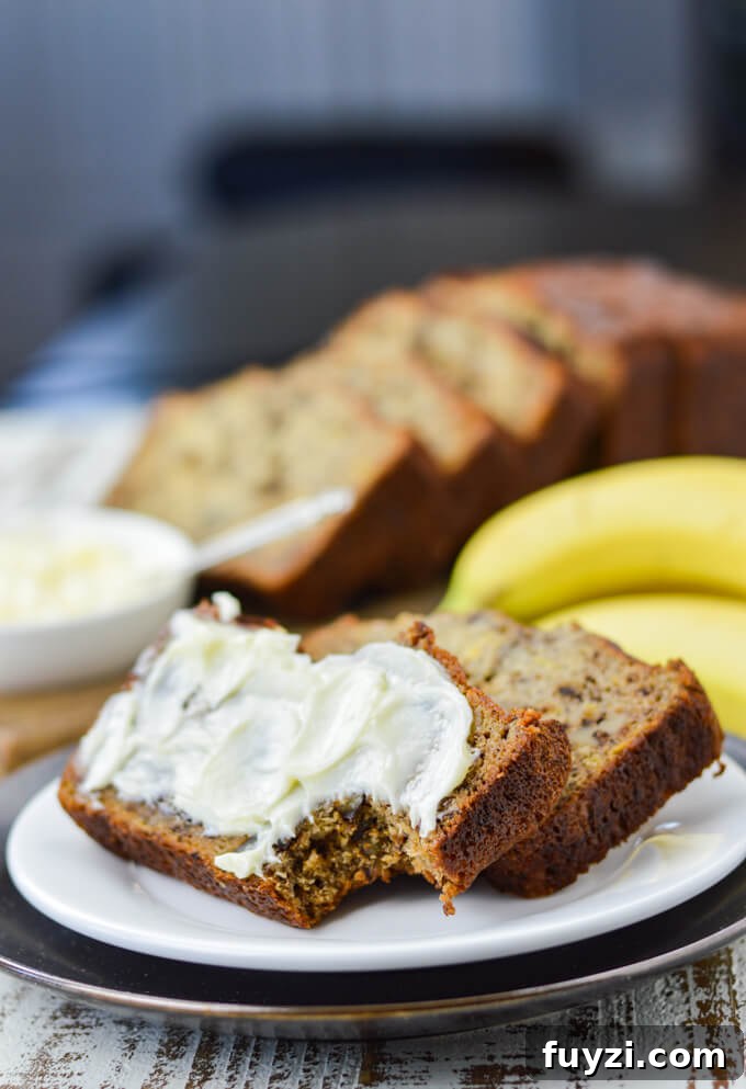 Moist Banana Nut Bread Recipe for Tender, Flavorful Loaves 2 Two slices of banana nut bread sit on a white plate. One has butter smeared on it and a bite taken out. Bananas, butter and more slices of bread sit in the background.