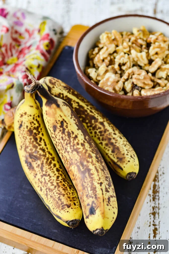 Moist Banana Nut Bread Recipe for Tender, Flavorful Loaves 3 Four ripe bananas sit on a black cutting board with a bowl of walnuts next to them.
