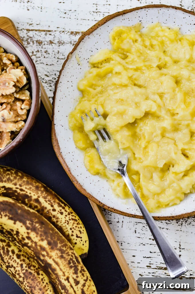 Moist Banana Nut Bread Recipe for Tender, Flavorful Loaves 4 A bowl of mashed bananas with a fork. A black cutting board has ripe bananas and a bowl of walnuts sitting next to the bowl.