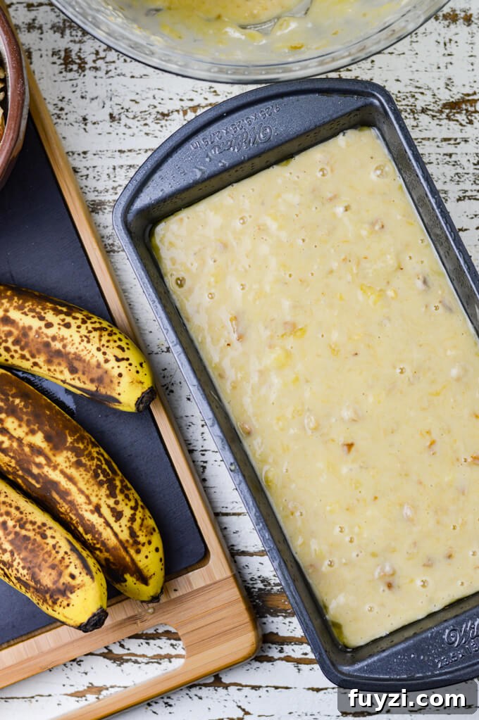 Moist Banana Nut Bread Recipe for Tender, Flavorful Loaves 6 A pan of banana nut bread batter with three ripe bananas on a black cutting board sits next to it.