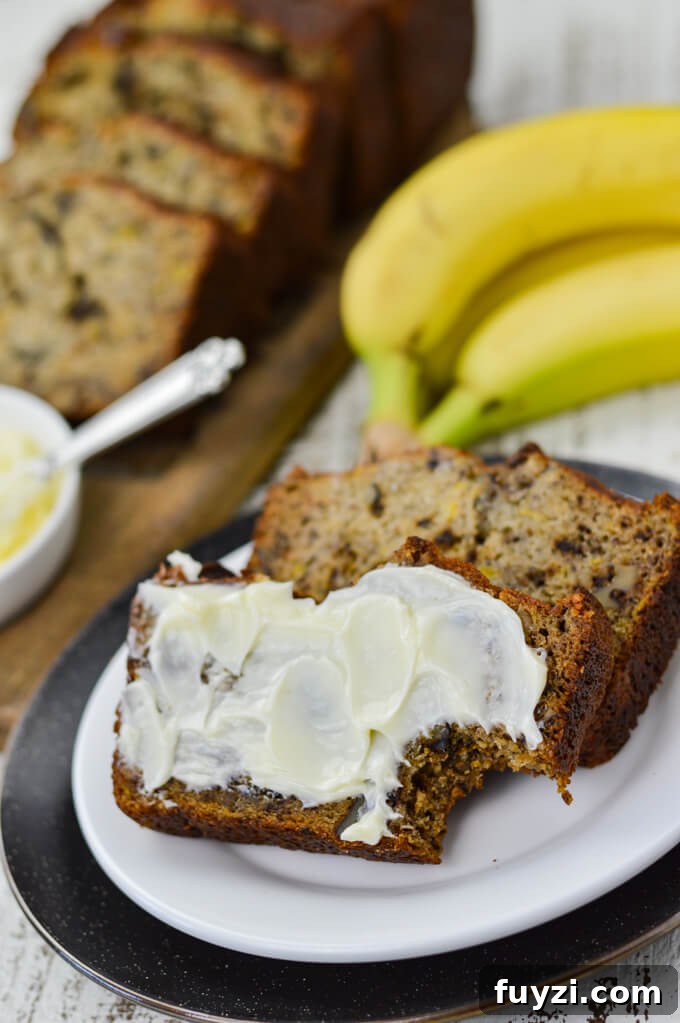 Moist Banana Nut Bread Recipe for Tender, Flavorful Loaves 7 Two slices of banana nut bread sit on a white plate. One has butter smeared on it and a bite taken out. Bananas, butter and more slices of bread sit in the background.