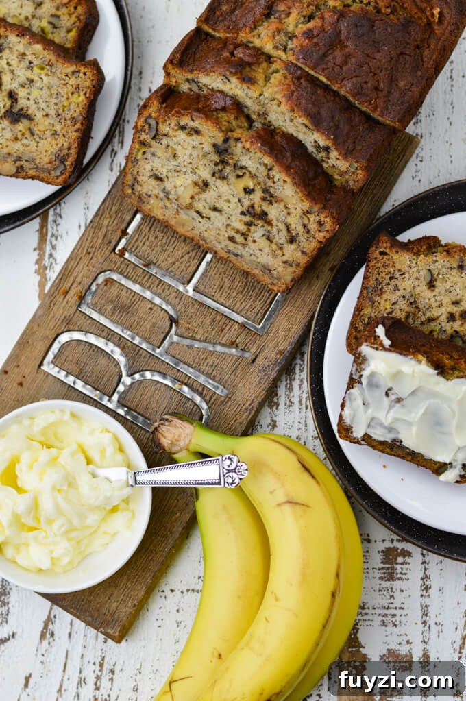Moist Banana Nut Bread Recipe for Tender, Flavorful Loaves 8 Slices of banana nut bread sit on a wooden cutting board with a small bowl of butter. Two slices of bread, one buttered and three bananas sit next to it.