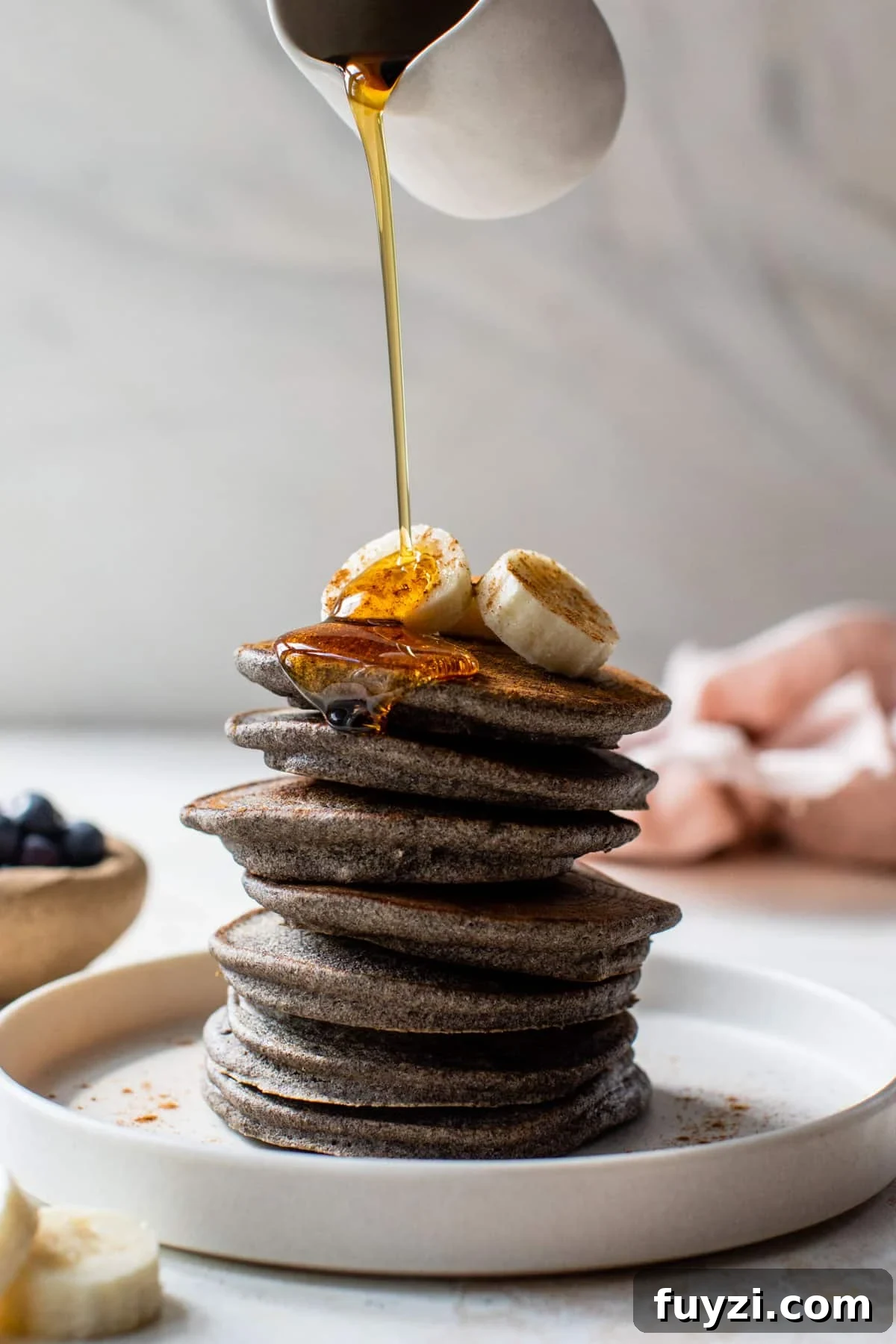 Fluffy Buckwheat Pancakes Recipe with Maple Syrup 2 buckwheat pancakes stacked on top of each other with bananas on top and maple syrup being poured over the top