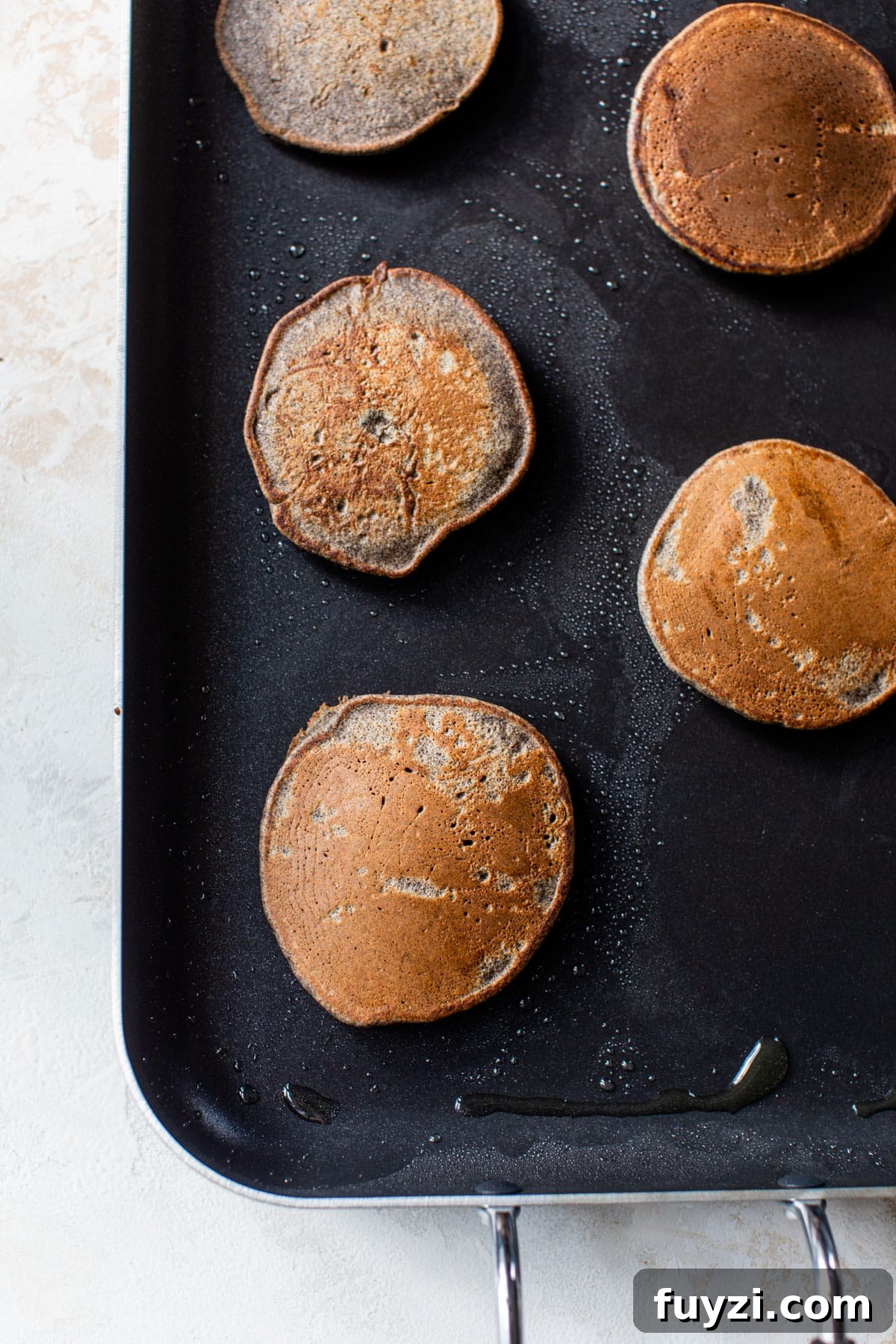 Fluffy Buckwheat Pancakes Recipe with Maple Syrup 4 pancakes cooking on a griddle