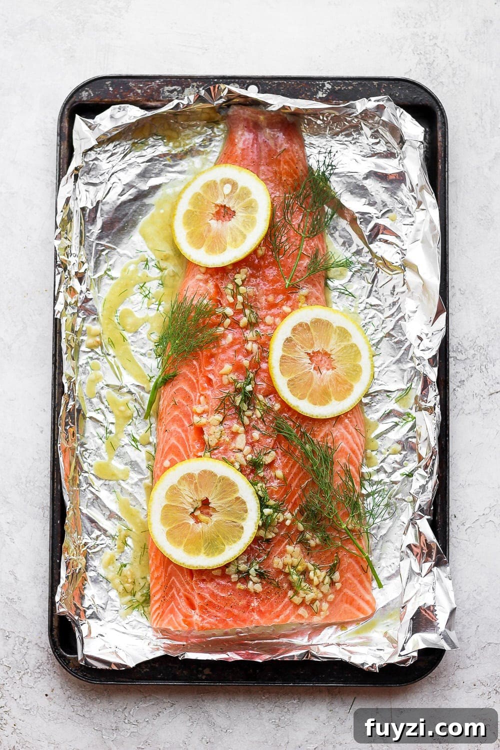 This perfectly cooked oven baked salmon in foil will give your family a delicious, healthy meal! It's naturally gluten-free and high-protein. large salmon fillet on tin foil with lemons, dill, and garlic