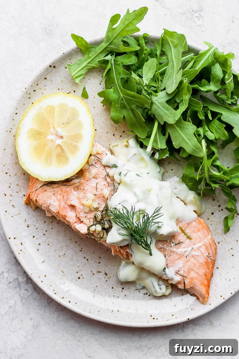 This baked salmon recipe is first marinated in a delicious lemon garlic sauce, then wrapped in tin foil and baked to a flakey perfection! salmon portion on plate with arugula, lemon, and tartar sauce